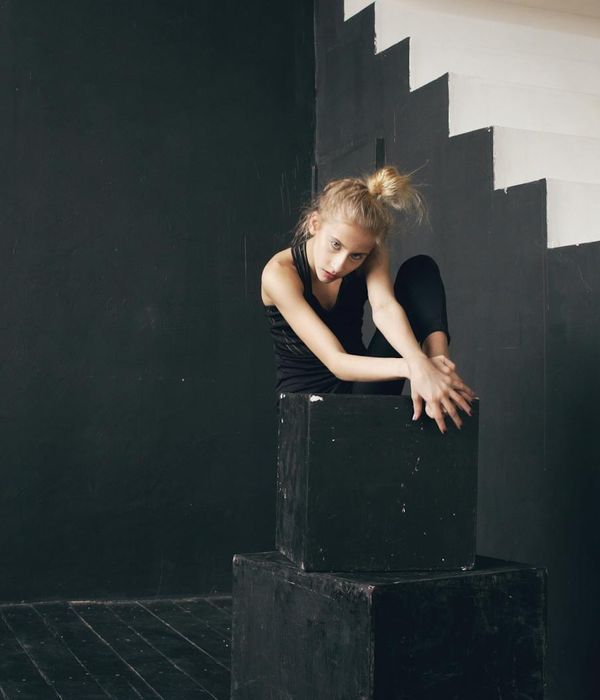 Woman performing a graceful flexibility exercise on a dark background.